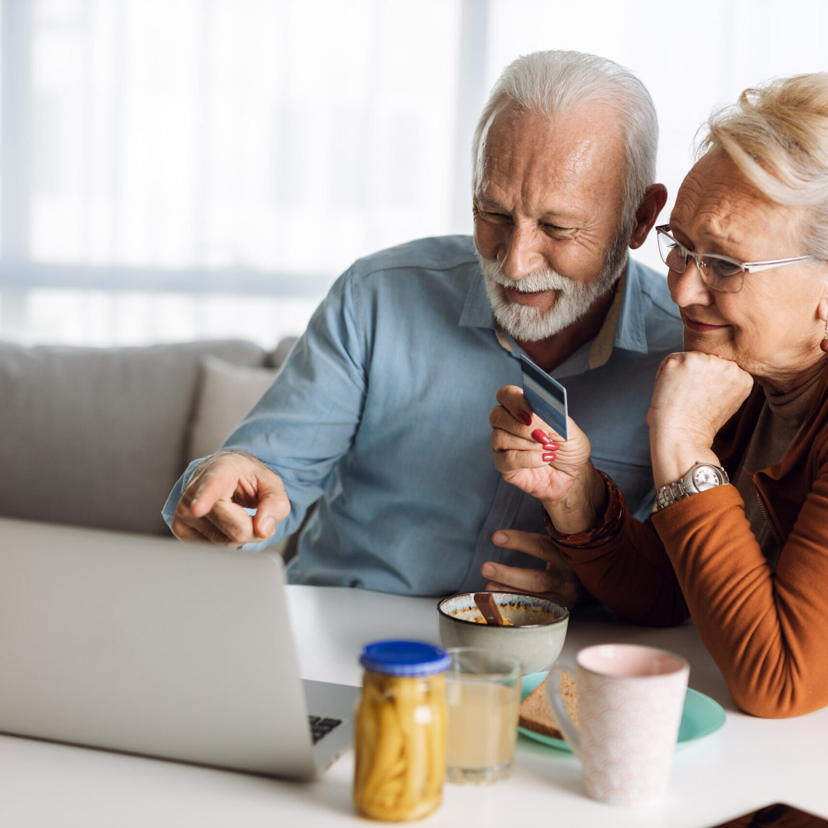 Older couple sitting at kitchen table looking at a laptop screen together